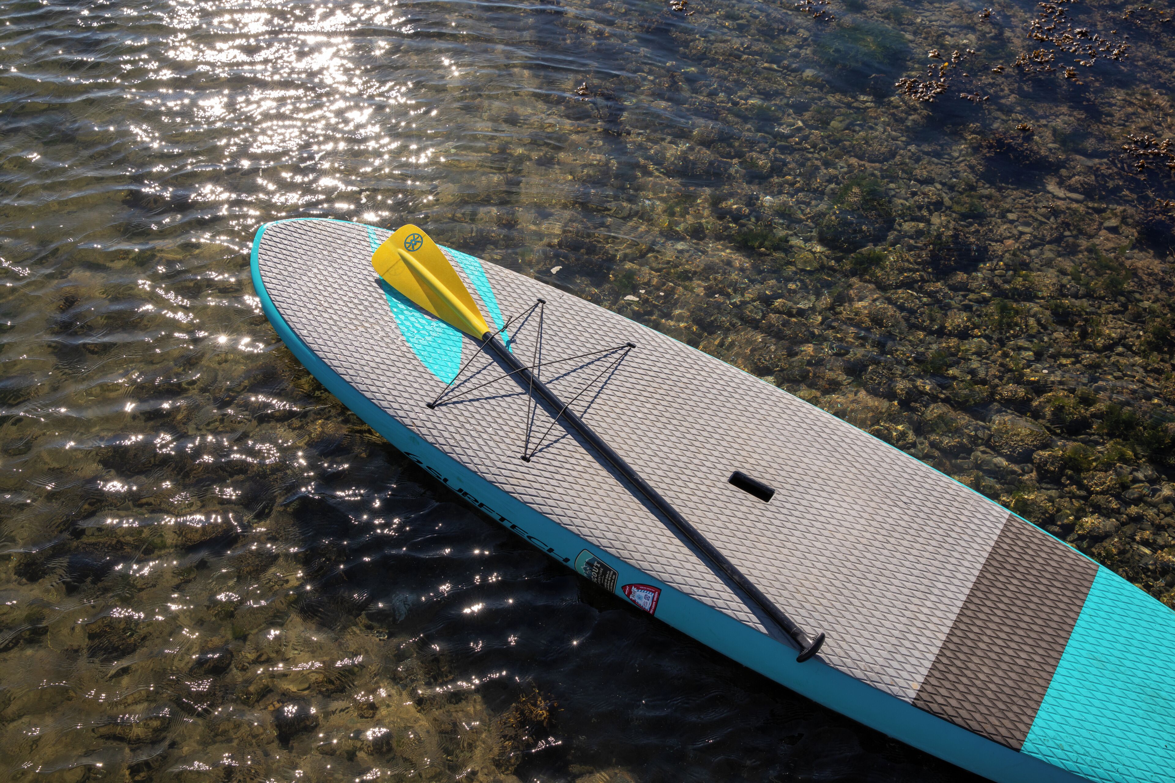 A paddleboard with a yellow paddle resting on it, floating on clear water.