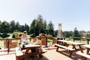 Una terraza de madera con mesas de picnic, una parrilla y una estructura alta con una luz en la parte superior.