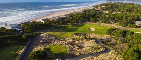 A golf course with a beach view, surrounded by houses and greenery.