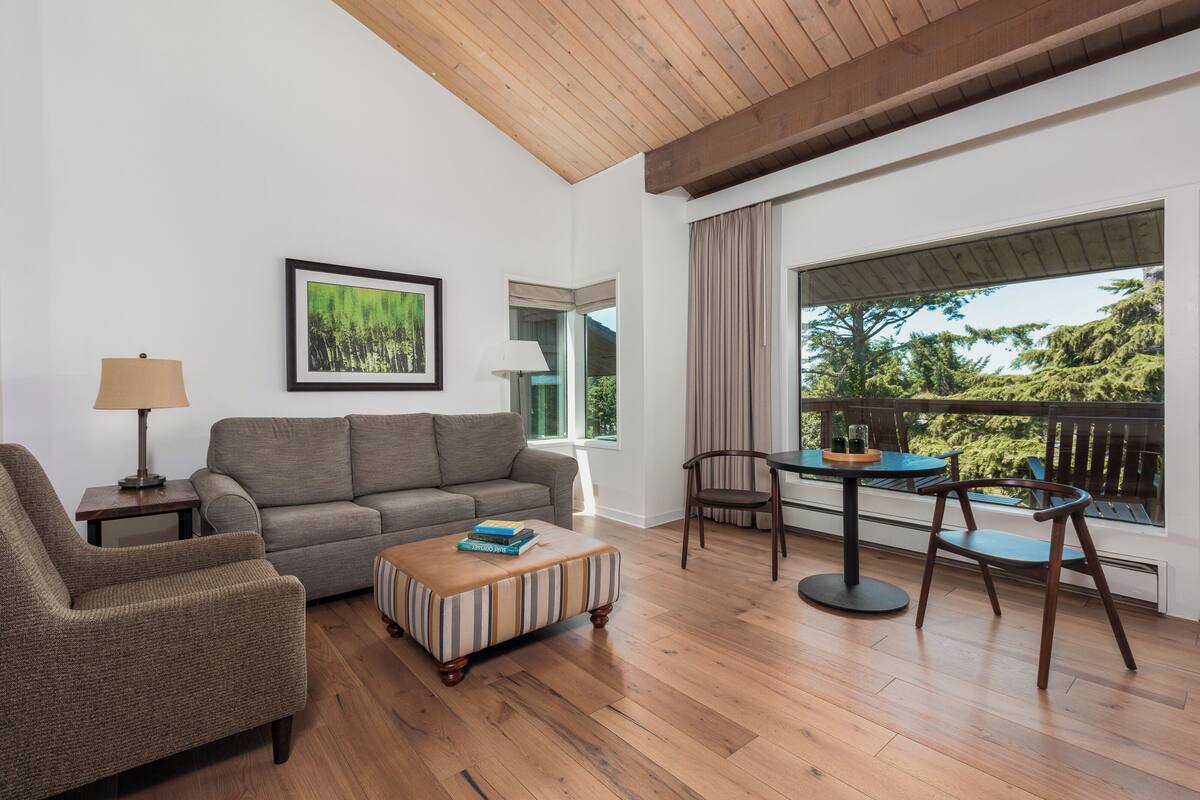 Un salon comprenant un canapé, un fauteuil, un pouf et une table avec des chaises.