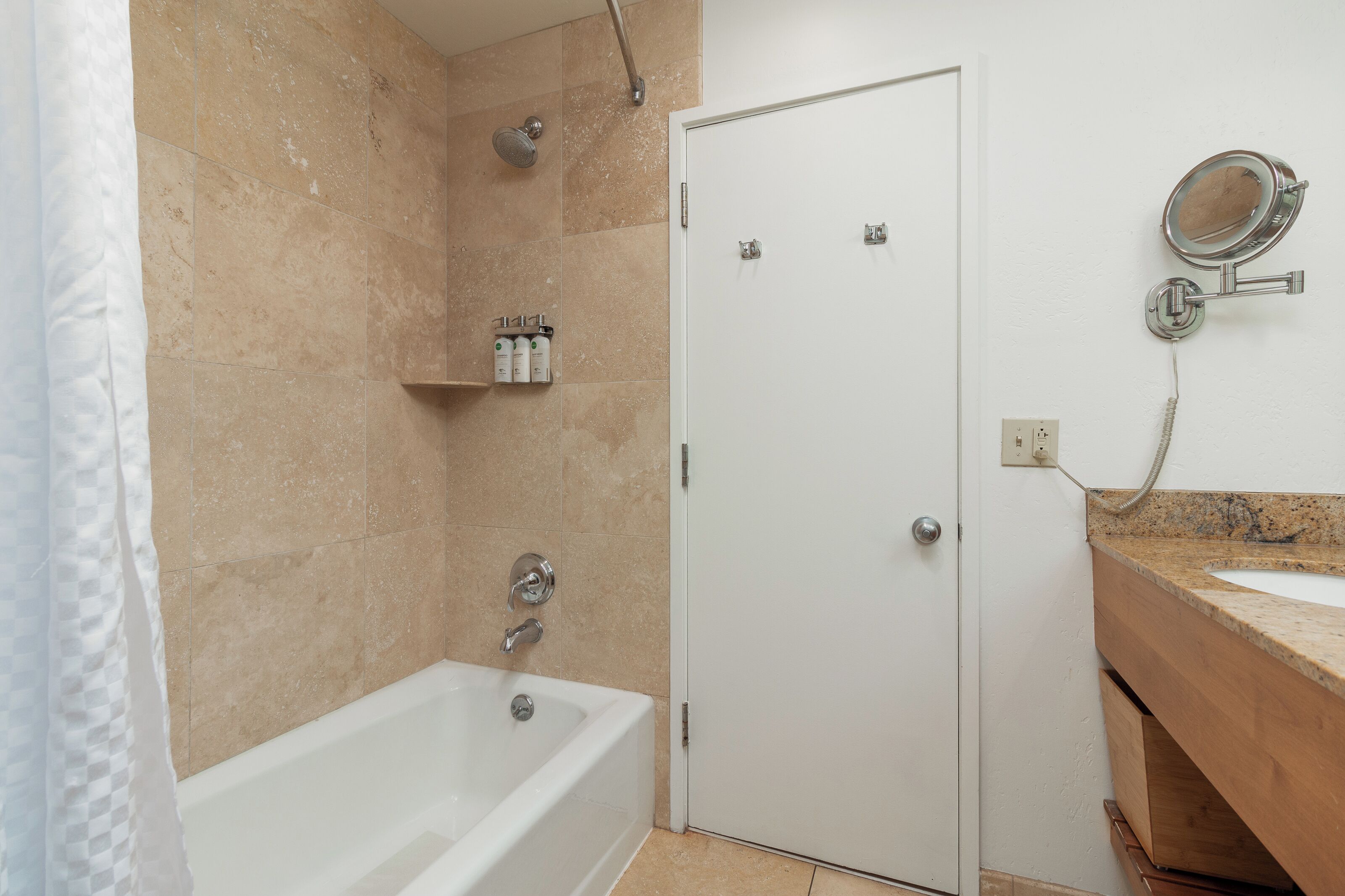 A bathroom with a bathtub, a shower, a vanity with a mirror, and toiletries on a shelf.