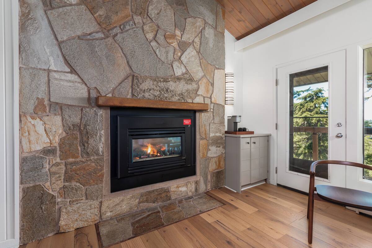 Une cheminée en pierre avec un feu de bois, un banc en bois et une porte donnant sur un balcon.