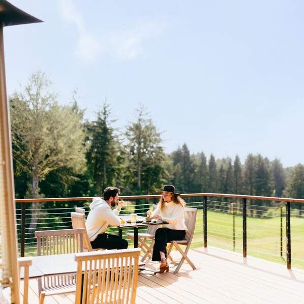 Una pareja cenando en una mesa al aire libre, con vistas a un bosque y un cielo despejado.
