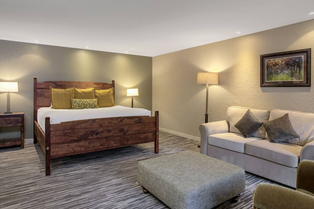 Une chambre d’hôtel avec un lit en bois, un canapé, une petite table et une lampe.