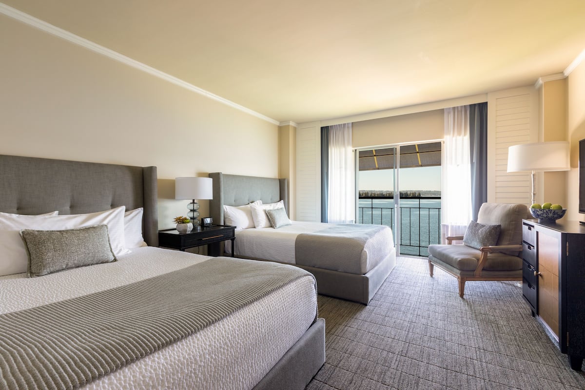Habitación de hotel con dos camas, una silla, un escritorio y vistas al exterior.