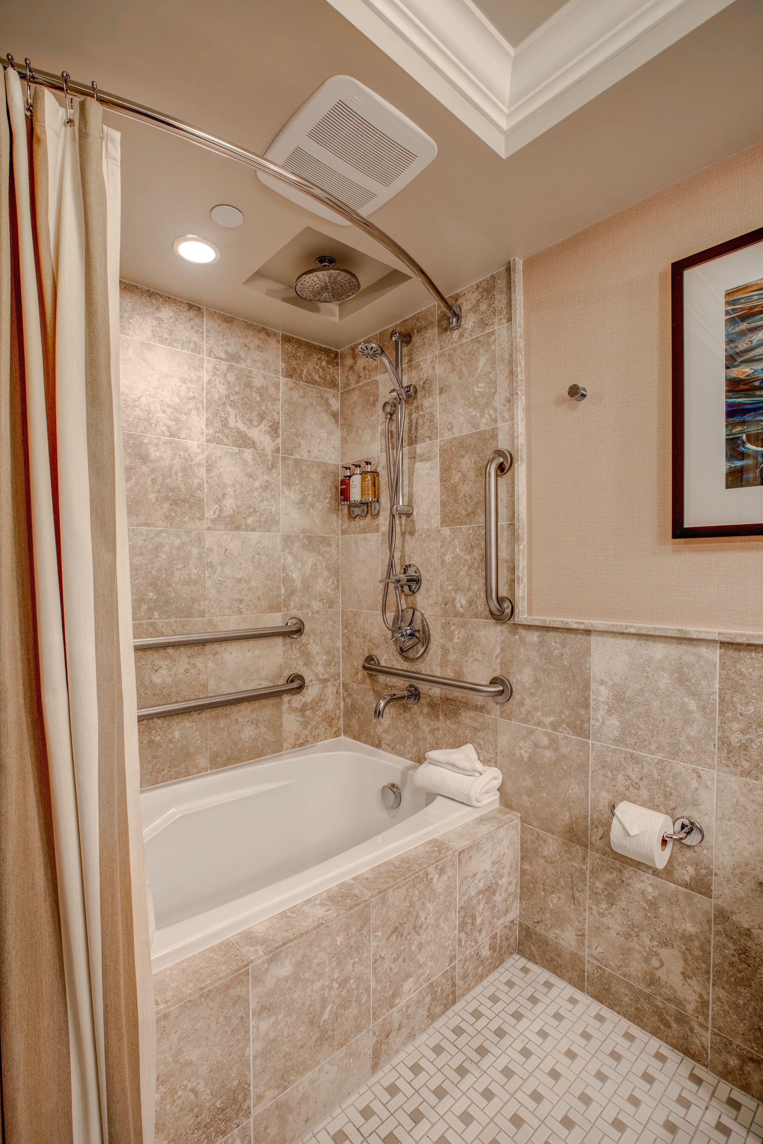 A bathroom with a bathtub, grab bars, a showerhead, and a framed picture on the wall.