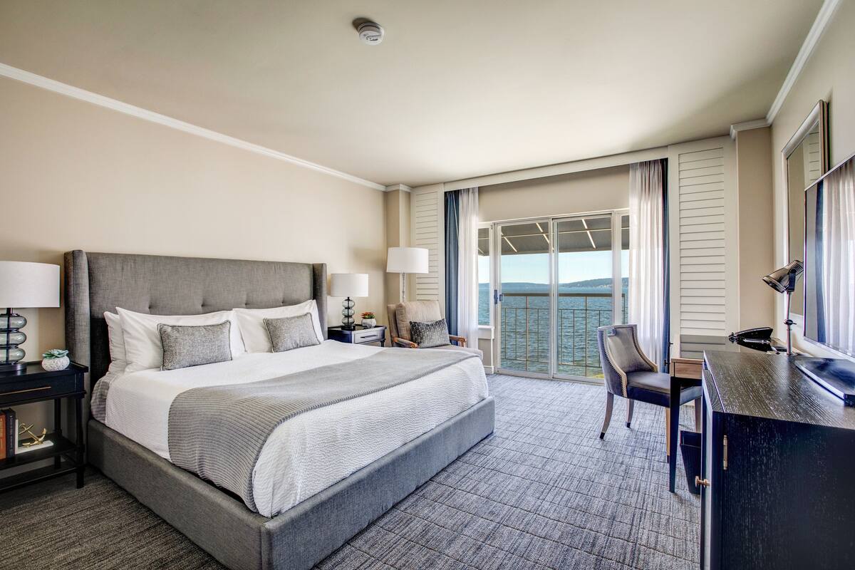 Habitación de hotel con una cama grande, un escritorio, una silla y un balcón con vistas.