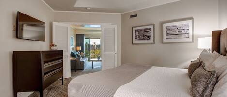 A bedroom with a large bed, a dresser, and a TV on the wall. There are framed pictures on the wall and a view of the outside through an open door.