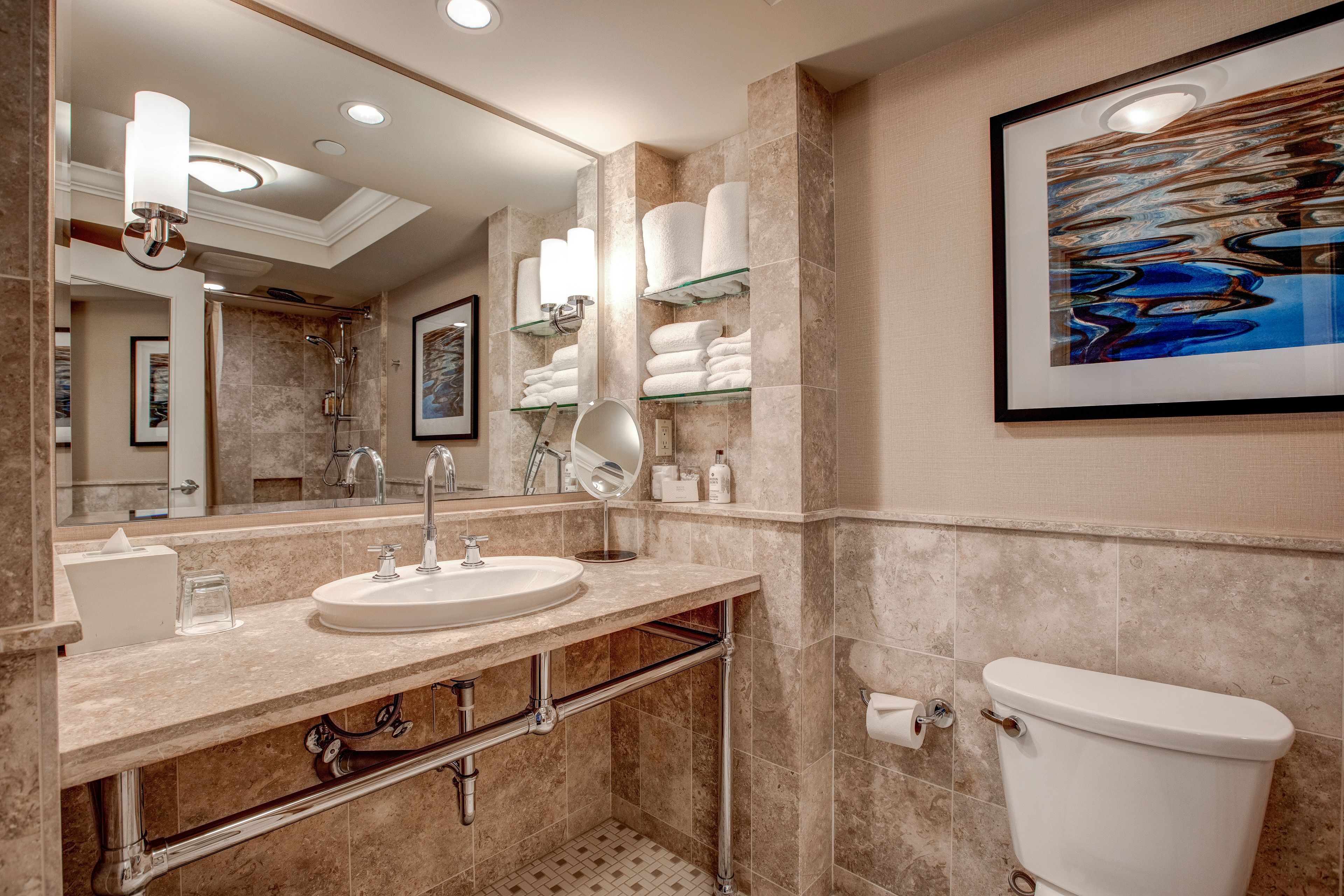 A modern bathroom with a large mirror, a sink, a toilet, and shelves with towels.