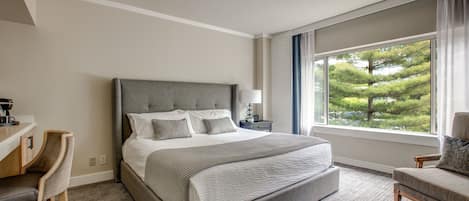 A hotel room with a large bed, a desk, a chair, and a window with a view of trees.