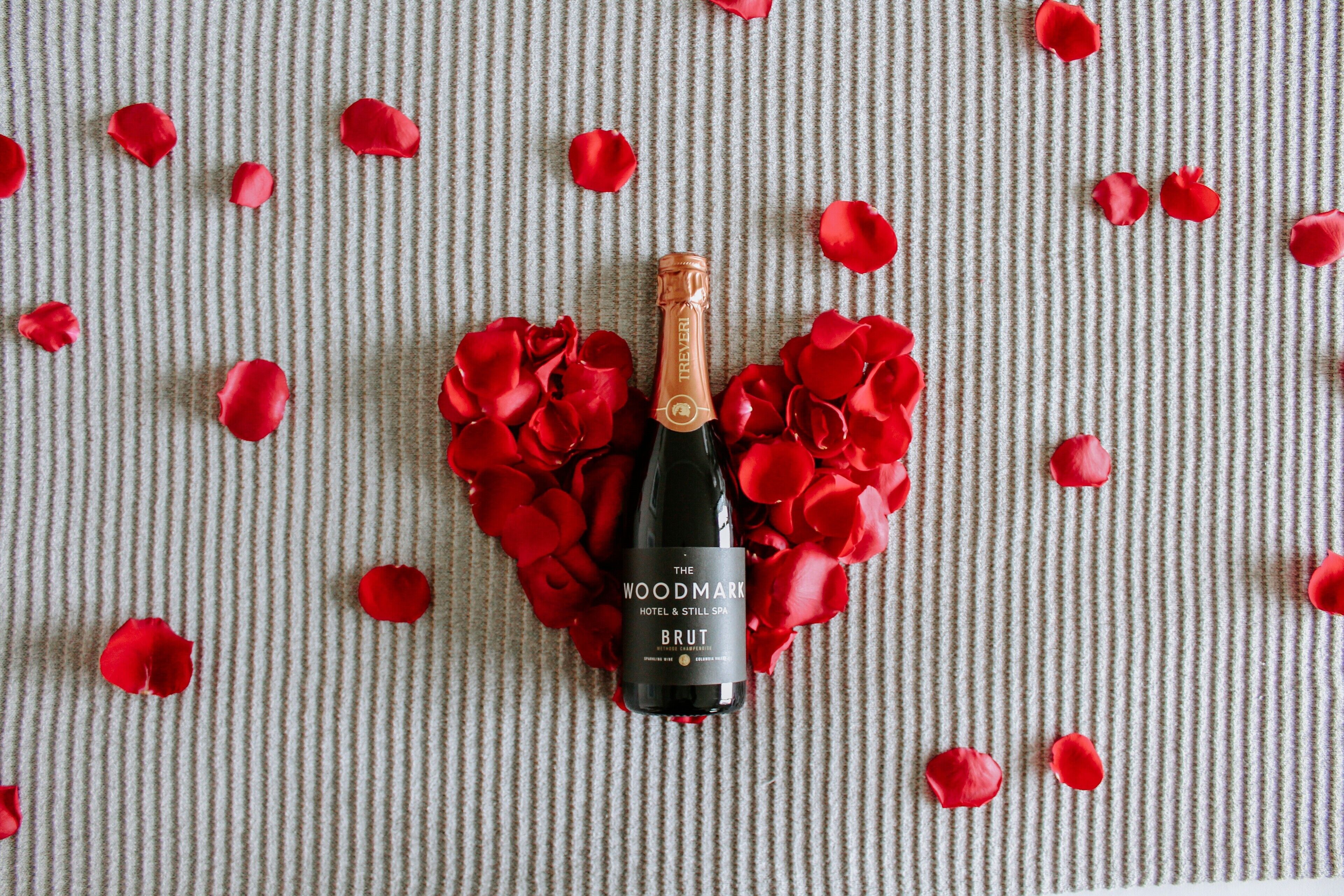 Une bouteille de champagne brut, entourée de pétales de roses rouges, posée sur une surface texturée.