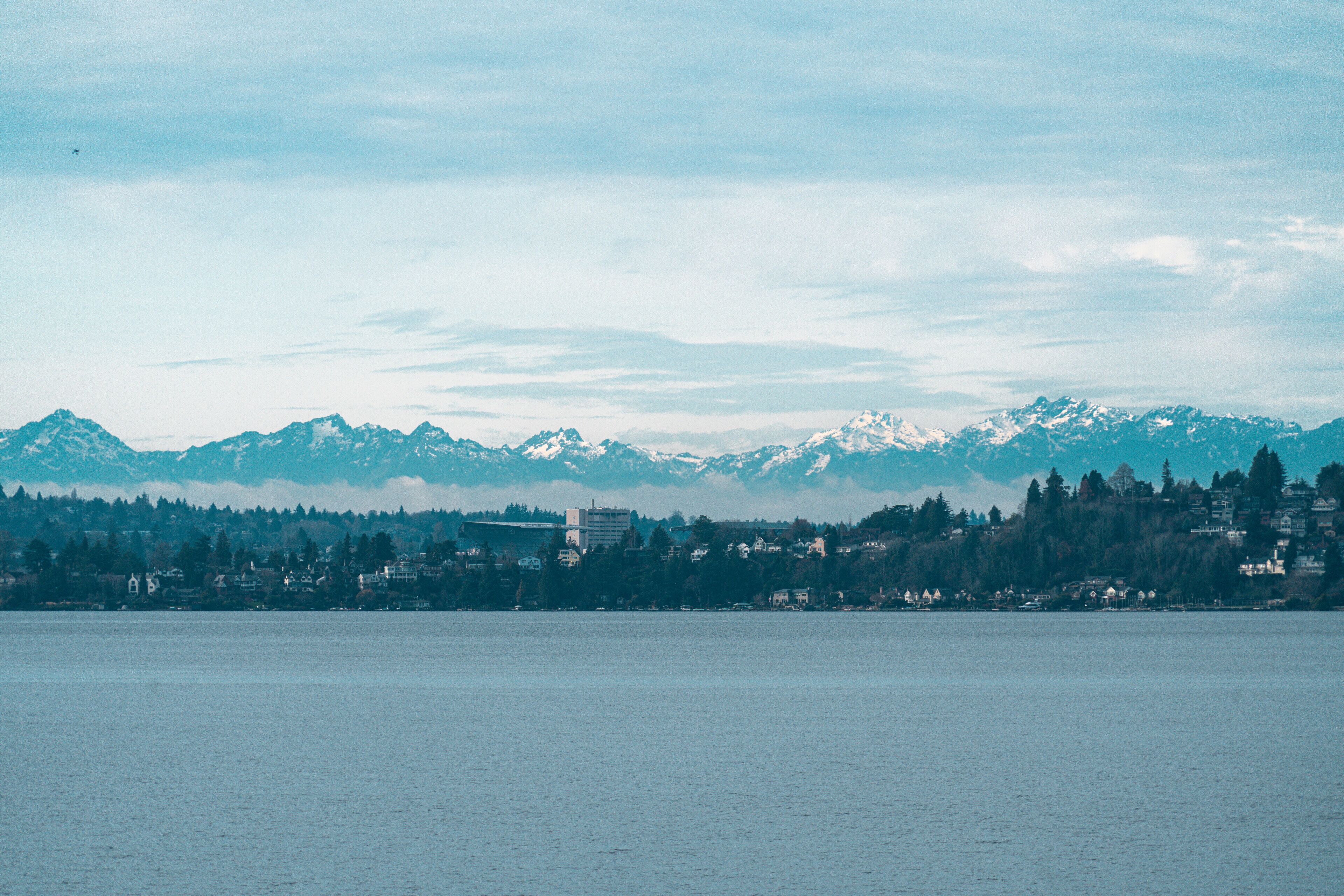 A coastal cityscape with mountains in the background and a calm body of water in the foreground.