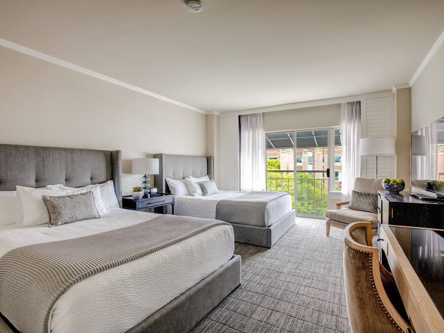 Habitación de hotel con dos camas, un escritorio, una silla, un televisor y un balcón con vistas.
