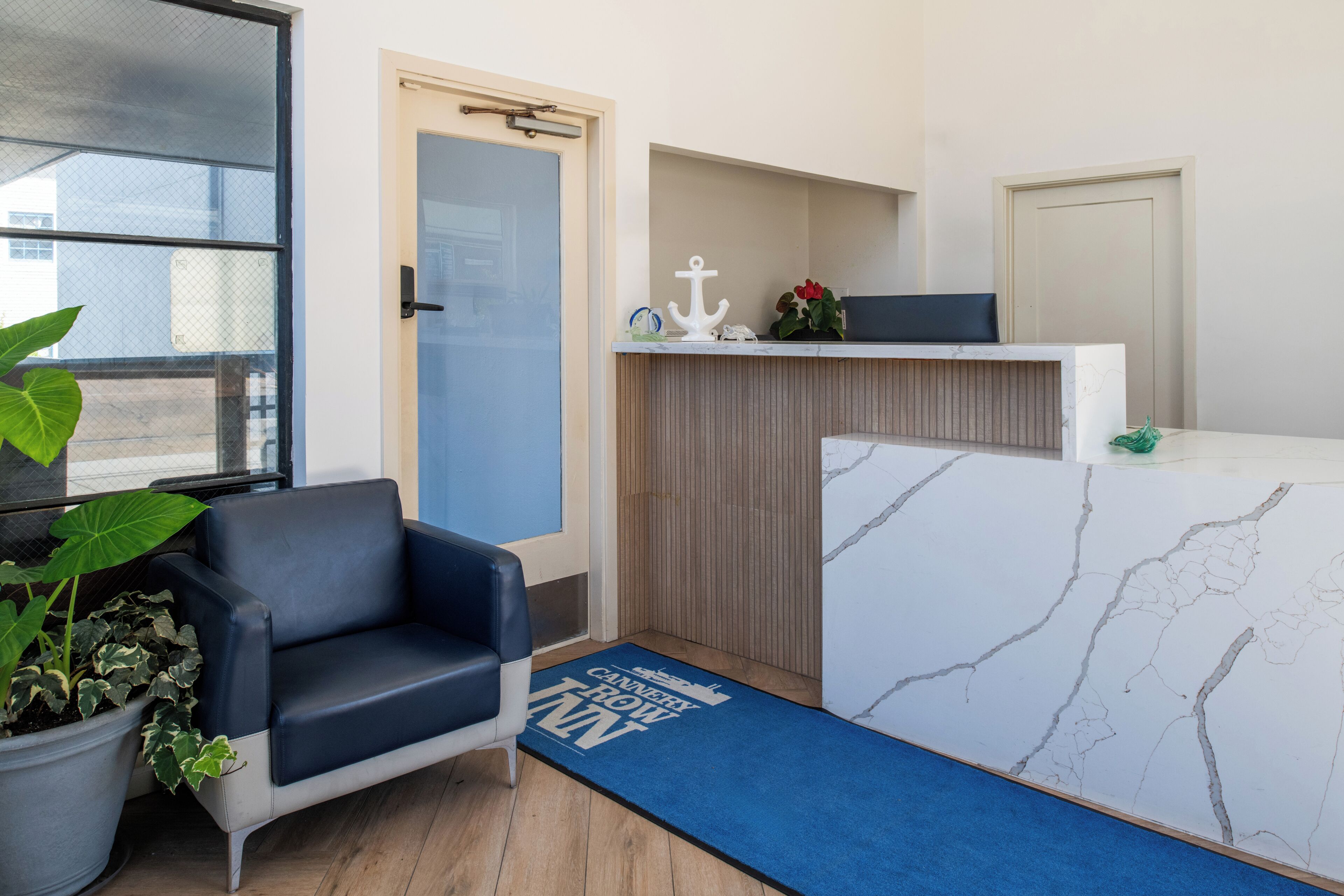 A reception area with a blue couch, a potted plant, a reception desk, and a blue mat with text.