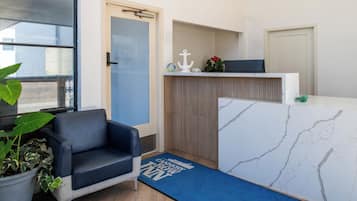 A reception area with a blue couch, a potted plant, a reception desk, and a blue mat with text.