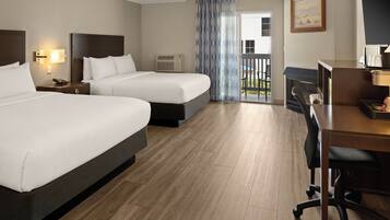 A hotel room with two beds, a desk, a chair, an air conditioning unit, and a view of the outdoors.