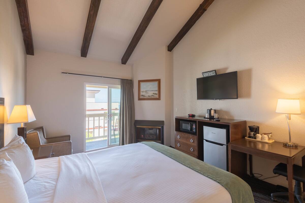 A hotel room with a large bed, a desk with a microwave, a television, and a view of the outside.