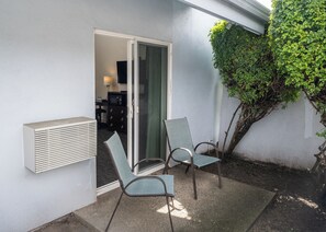 A patio with two chairs, a heater, and a door leading to a room with a TV and a desk.