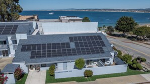A modern building with solar panels on the roof, a sign reading 'CANNERY ROW INN,' and a view of the ocean.
