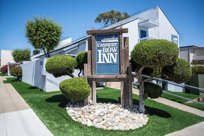 A Cannery Row Inn sign with a wooden structure, surrounded by well-manicured hedges and a gravel path.