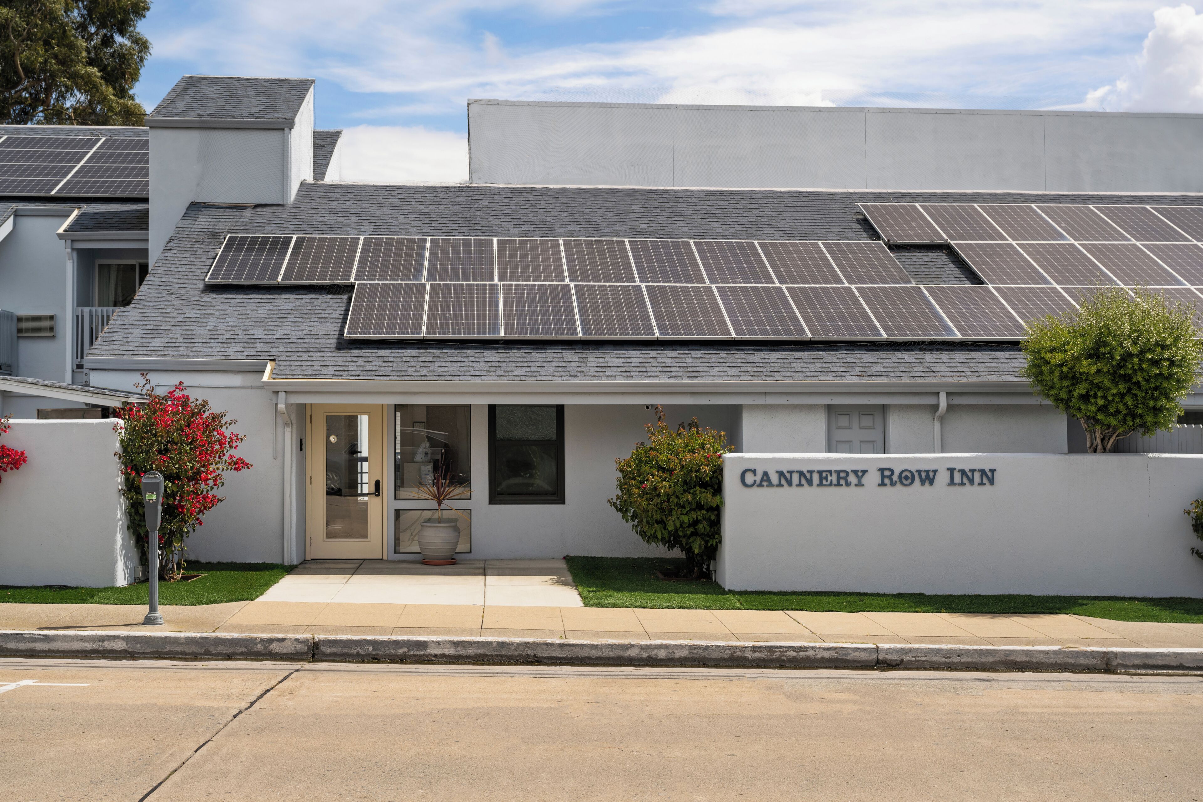 Ein Gebäude mit Solaranlage auf dem Dach, einem Schild mit der Aufschrift 'CANNERY ROW INN' und einem kleinen Eingang mit Tür und Stufen.