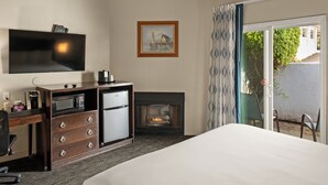 A hotel room with a bed, a desk with a microwave, a fireplace, a television mounted on the wall, and a view of the outside.