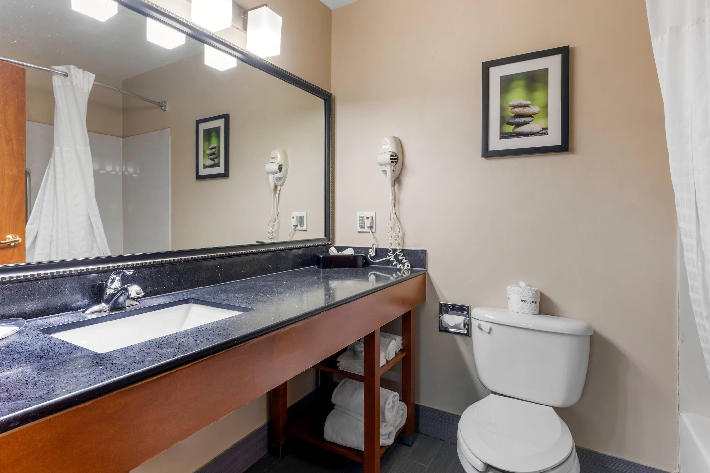 A bathroom with a large mirror, two hair dryers, a sink, and a toilet.