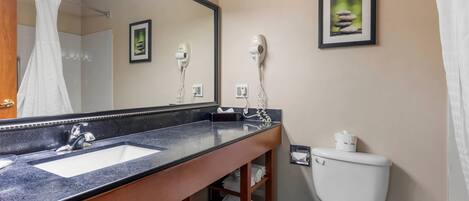 A bathroom with a large mirror, two hair dryers, a sink, and a toilet.