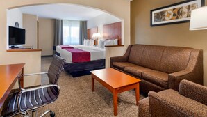 A hotel room with a bed, a sofa, a desk with a chair, a TV, and a lamp. - Comfort Suites North Dallas (Dallas)