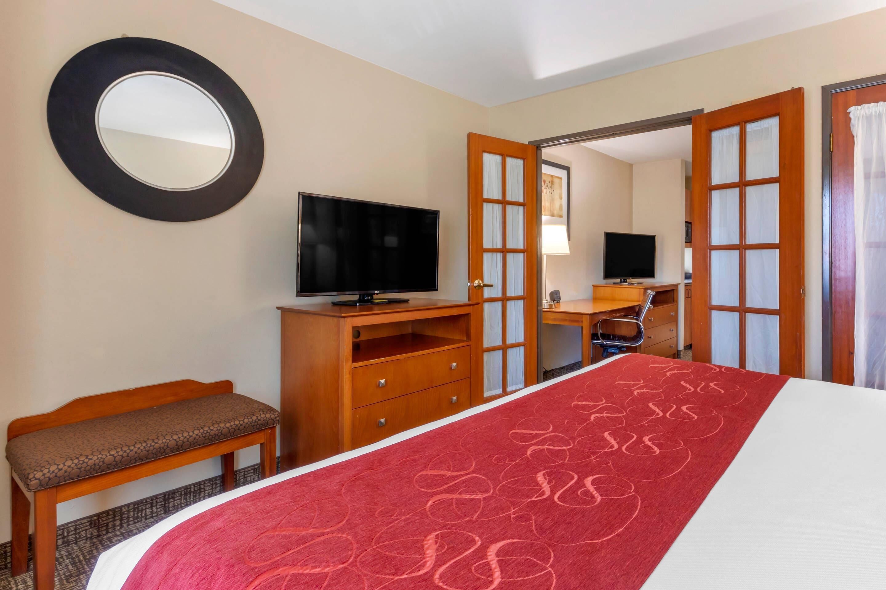 Habitación de hotel con cama, televisión, banco de madera, escritorio y espejo.