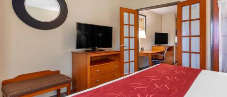 Habitación de hotel con cama, televisión, banco de madera, escritorio y espejo.