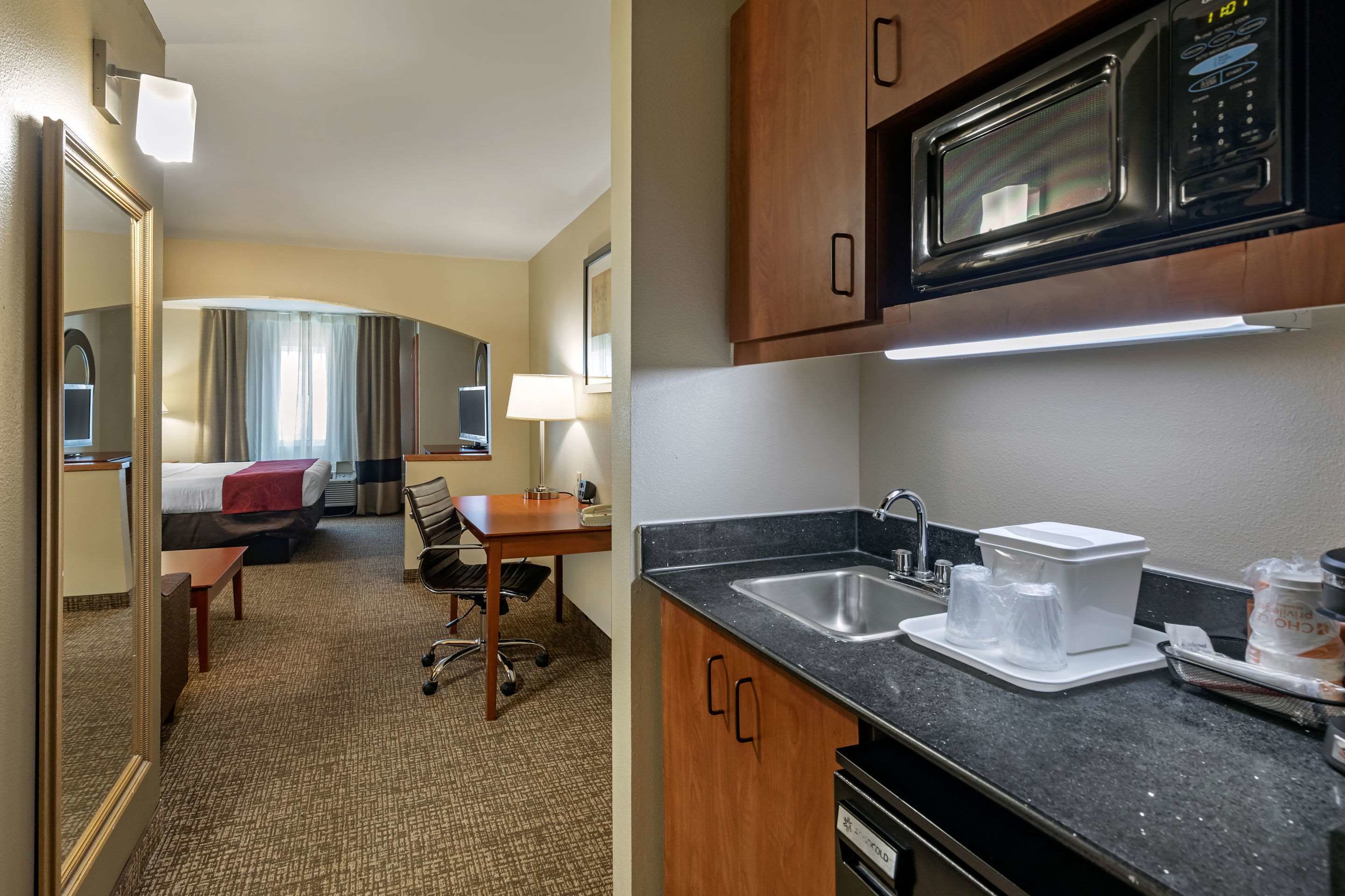 Ein Hotelzimmer mit Bett, Schreibtisch, Stuhl und einer Küchenzeile mit Mikrowelle, Spüle und Stauraumschränken.