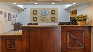 A reception desk with a wooden finish, a sign reading "Comfort Suites," and a welcome sign with flowers. - Comfort Suites North Dallas (Dallas)