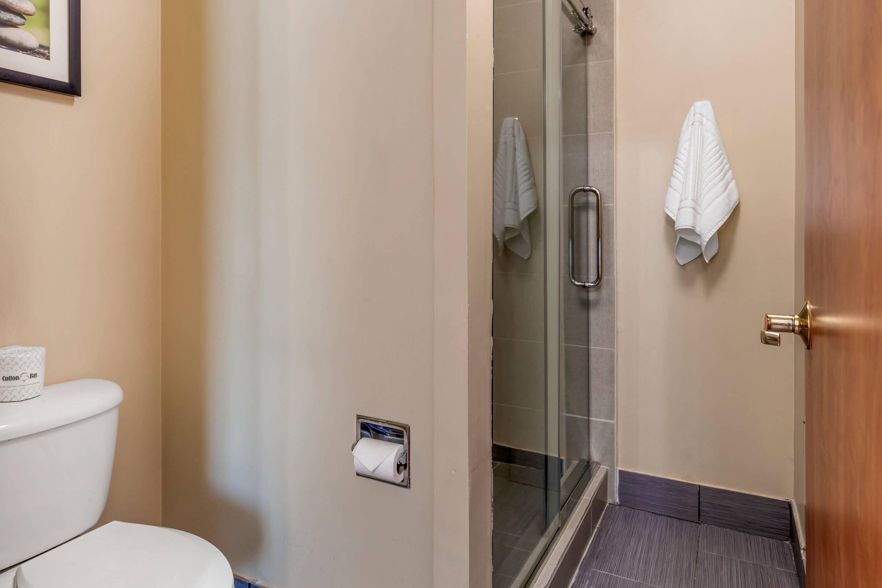 Une salle de bain équipée de toilettes, d’une douche à parois de verre et de deux serviettes accrochées au mur.