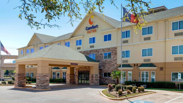 A Comfort Suites hotel with a brick facade, multiple windows, and a covered entrance. - Comfort Suites North Dallas (Dallas)