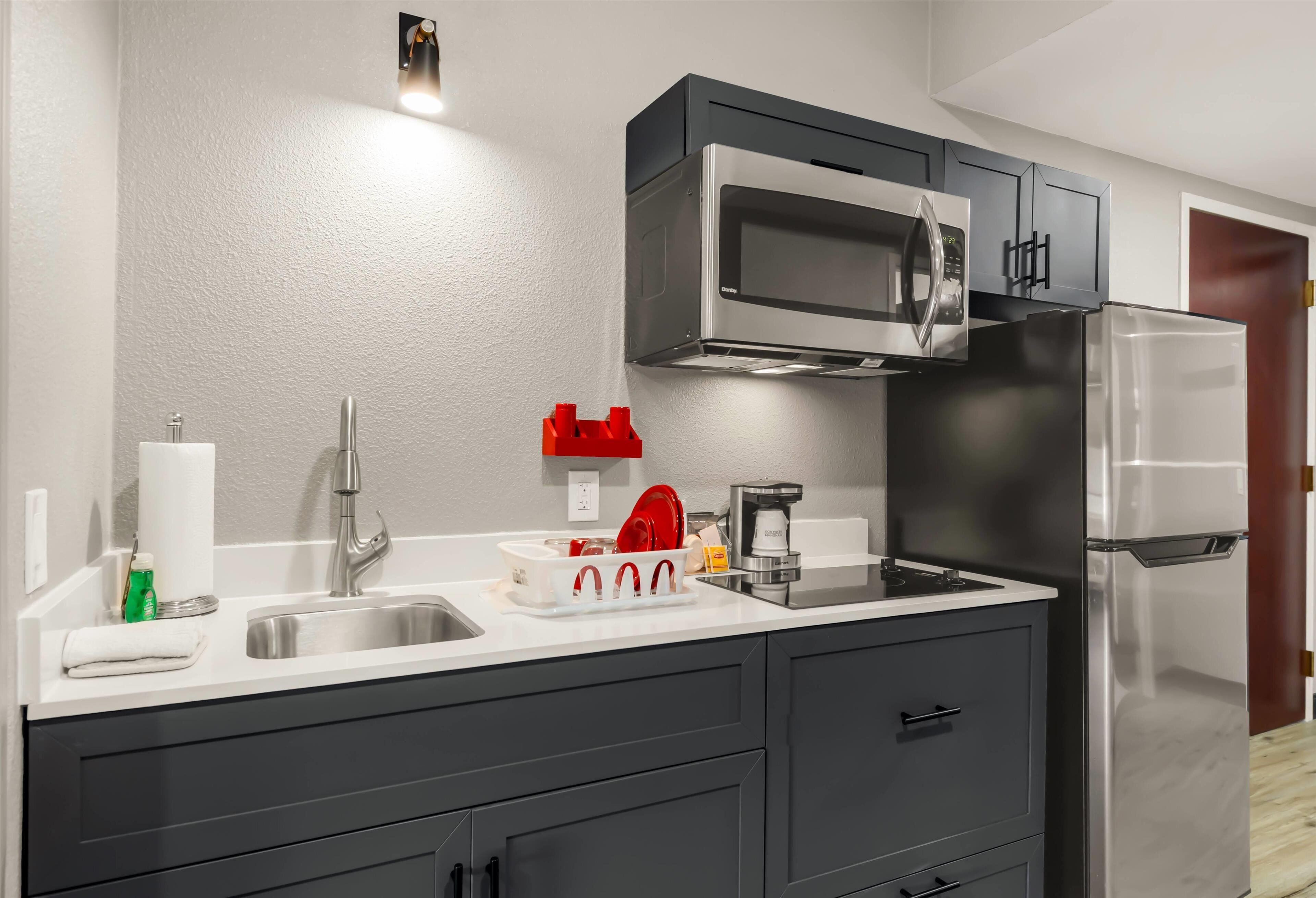 Una cocina moderna con un refrigerador de acero inoxidable, un microondas y una cafetera sobre la encimera.