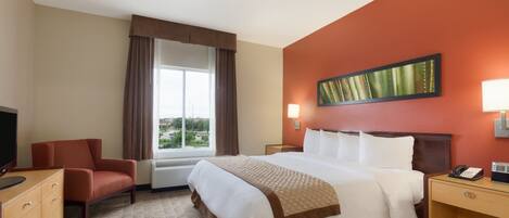 A hotel room with a large bed, a desk, a chair, a television, and a window with curtains.