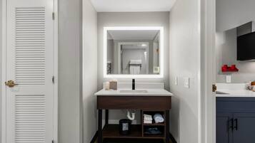 Une salle de bain avec une porte blanche, un meuble-lavabo en bois avec un miroir, un évier et un placard contenant des serviettes.