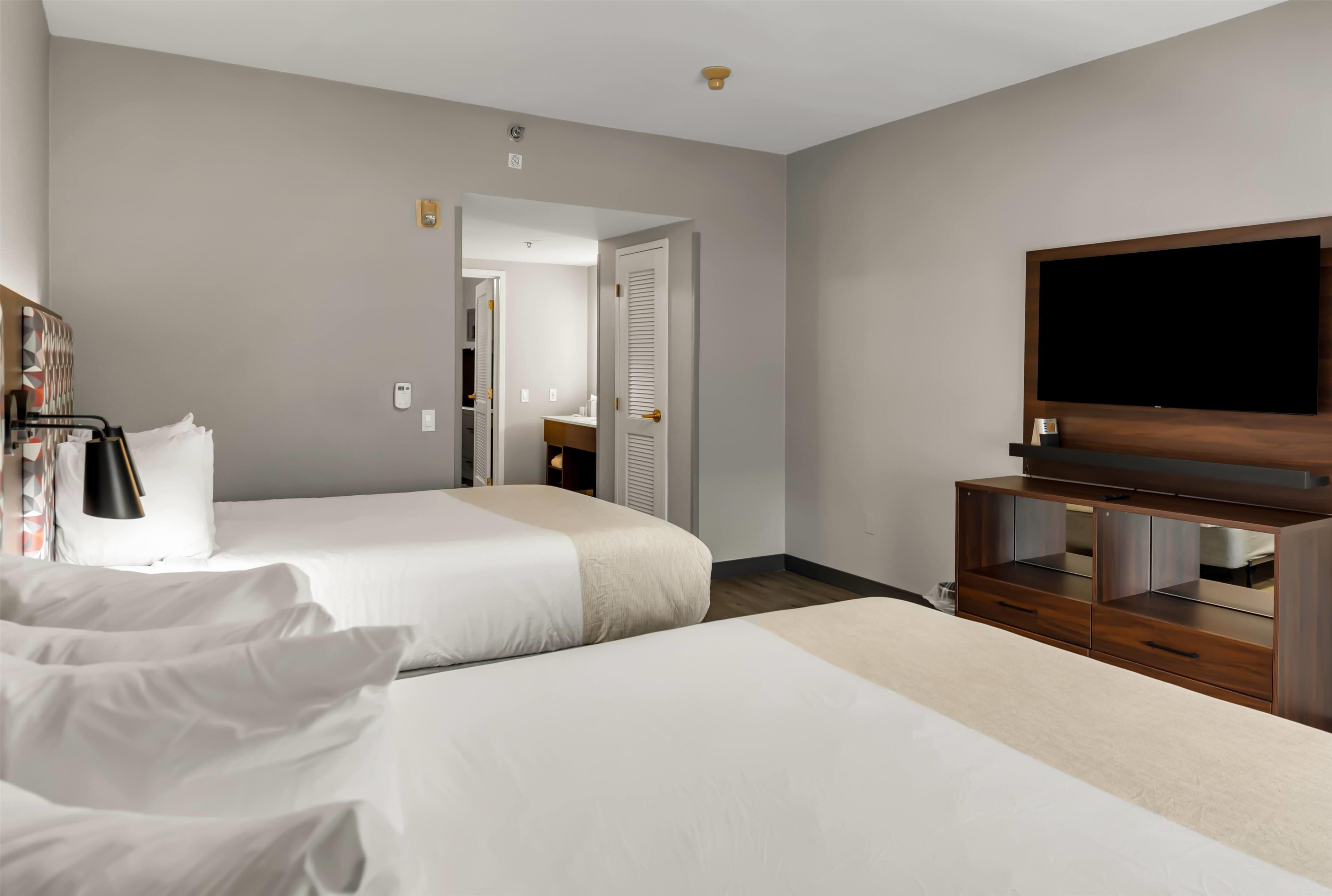 A hotel room with two beds, a TV, a wardrobe, and a bathroom visible through an open door.