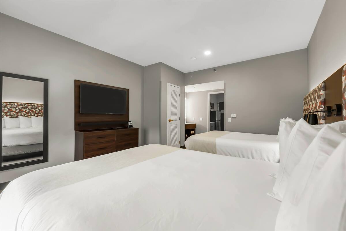 Una habitación de hotel con dos camas, un televisor de pantalla plana, un aparador y un espejo.