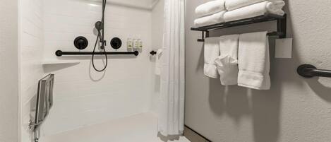 Une salle de bain moderne avec une douche à l’italienne, un porte-serviettes où les serviettes sont soigneusement pliées, et un distributeur de savon fixé au mur.