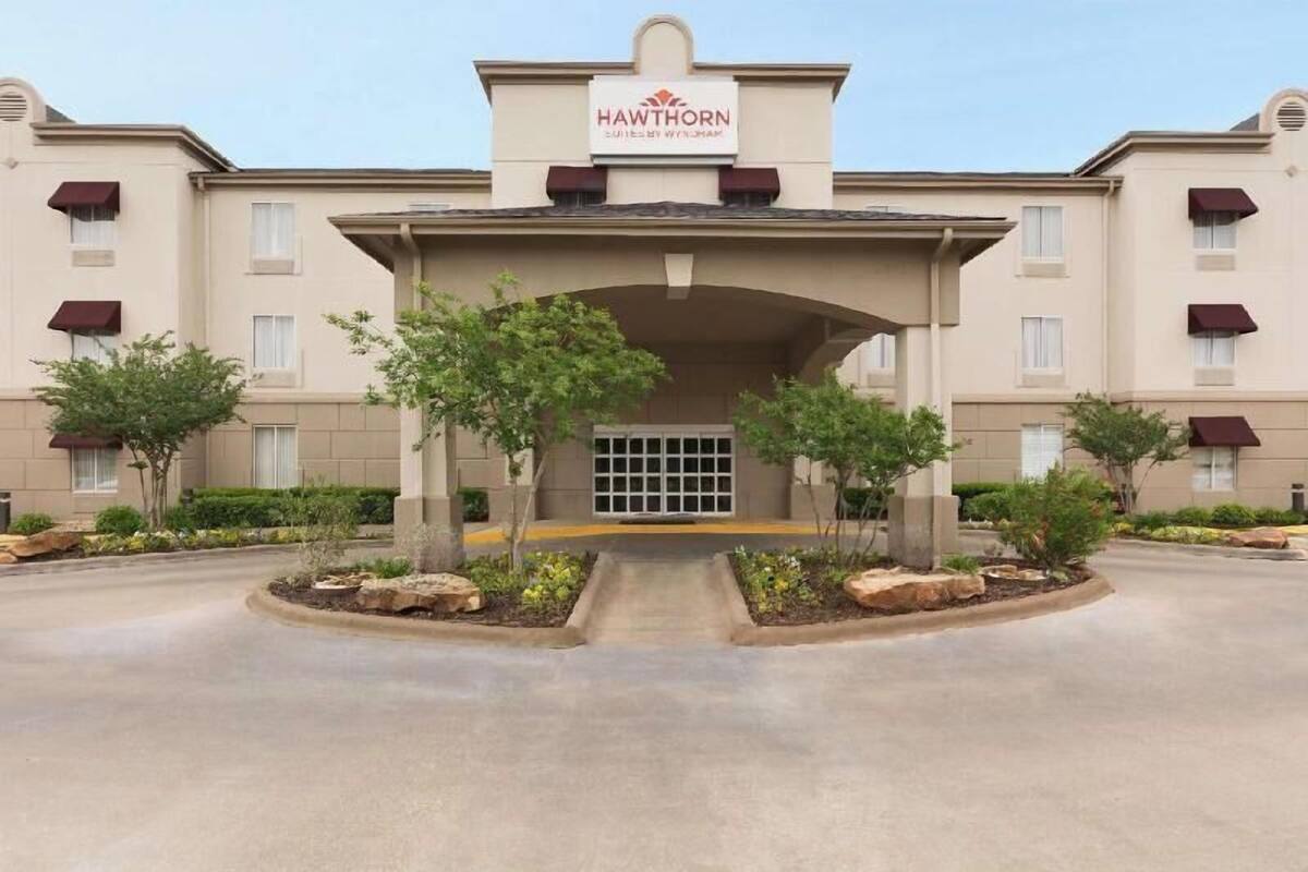 Entrada de un hotel con un letrero que dice 'Hawthorn', un corredor cubierto y áreas ajardinadas con árboles y arbustos.