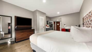 Een moderne hotelkamer met een groot bed, een aan de muur bevestigde televisie, een garderobe, een kleine kitchenette en een badkamer die door een geopende deur zichtbaar is.