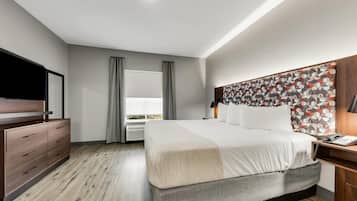 Habitación de hotel moderna con una cama grande, un aparador de madera, un televisor de pantalla plana y una ventana con cortinas.