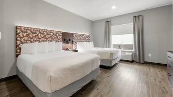 Una habitación de hotel con una cama grande, una cama más pequeña, un aparador, una ventana con cortinas y una pared con diseño geométrico.