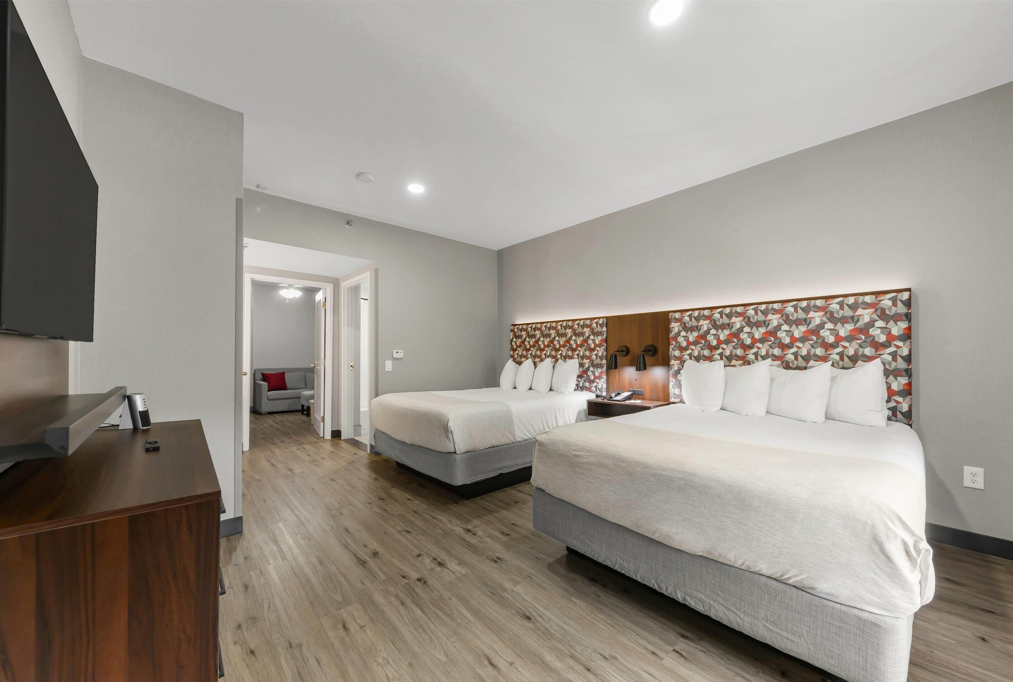 Camera d'albergo con due letti, televisore, scrivania e testiera a motivi decorativi.