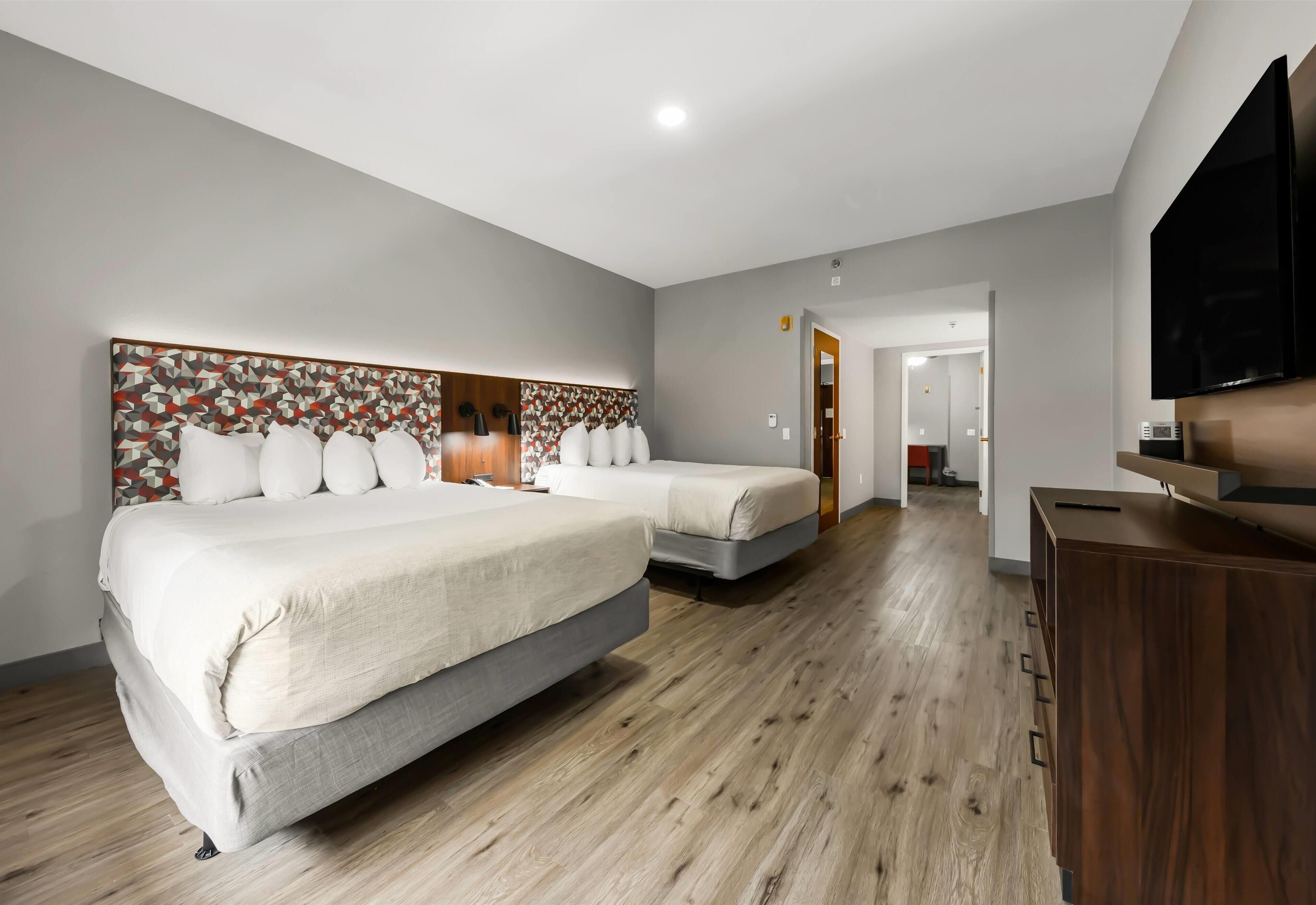 Une chambre d’hôtel avec deux lits, un plancher en bois, une télévision et une armoire en bois.