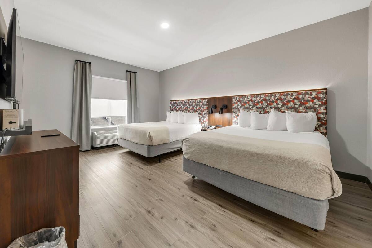 Una habitación de hotel con dos camas, un escritorio, un televisor y un ventanal con cortinas.