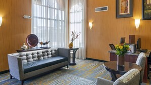 A hotel room with a sofa, a small table with a vase of flowers, a desk with a computer, and a large window with sheer curtains. - Best Western Plus Fresno Inn (Fresno)