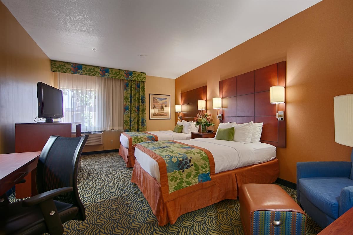 A hotel room with two beds, a desk with a chair, a TV, and a sofa.
